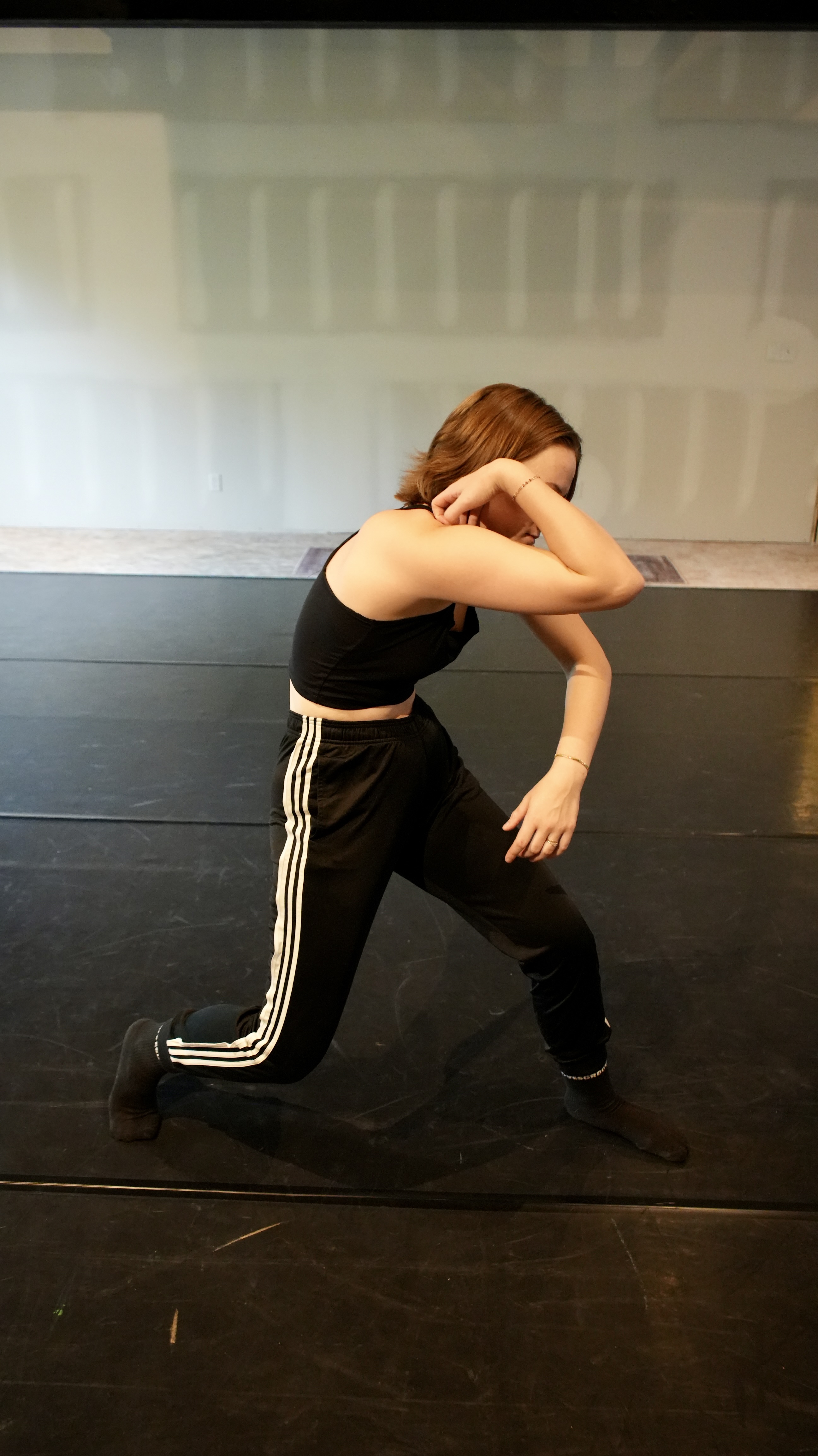 A young woman with short brown hair, dressed in a black sports bra and black pants with white stripes down the side, exhib...