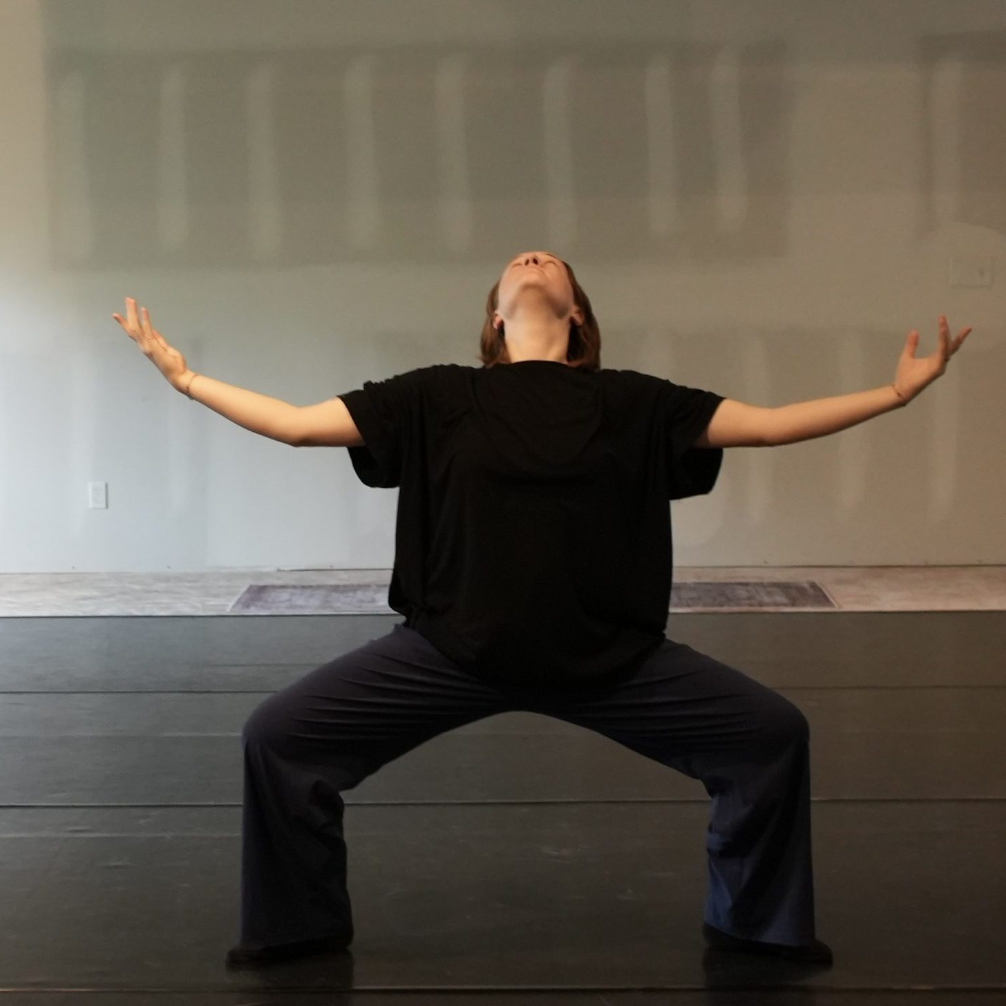 A man in a crouched position with arms stretched out, squatting in a dance studio.